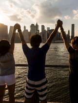 friends excitedly raise their hands as they look at the new york city skyline